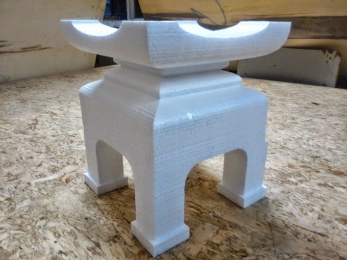 A white foam pedestal with a curved saddle top and arched legs, cut in a simple 2-axis hot-wire pass, on an OSB workbench