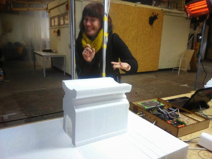An early FoamCube cut: a white foam architectural column capital on the machine bed, with the maker and the RAMPS controller electronics in the workshop behind