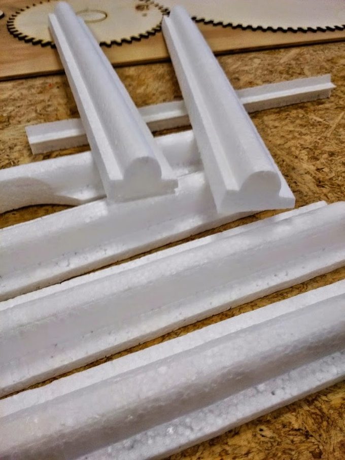 Lengths of decorative EPS crown and cornice moulding profiles (ogee and half-round) cut on the FoamCube, on a workbench
