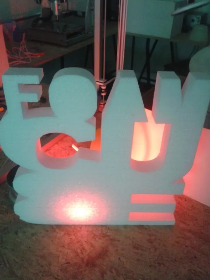 Flache 2-Achsen-Hot-Wire-Foam-Buchstaben, rückseitig mit warmem Licht beleuchtet, auf dem Maschinenbett
